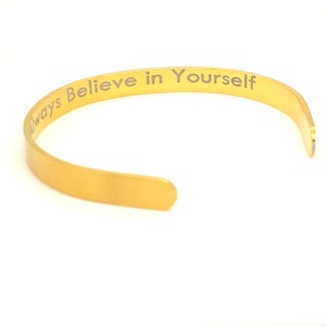 Puede incluir: Pulsera de brazalete dorada con la inscripción "Always Believe in Yourself".