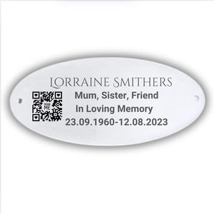 May include: White oval metal plaque with black text that reads "Lorraine Smithers, Mum, Sister, Friend, In Loving Memory, 23.09.1960-12.08.2023". A black and white QR code is on the left side of the plaque.