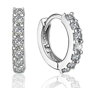 May include: A pair of silver hoop earrings with a row of clear cubic zirconia stones around the edge.