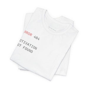 May include: A white short-sleeved t-shirt featuring the red and black text ERROR 404 MOTIVATION NOT FOUND printed on the front. The shirt has a crew neckline and is folded to display the graphic design clearly against the plain white fabric.
