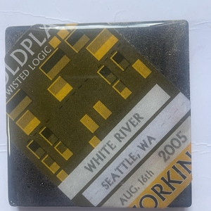 May include: A black and yellow square coaster with a concert ticket design. The ticket reads "White River, Seattle, WA, Aug. 16th, 2005" and "Sold Out" with the band name "The Used" printed on the bottom.