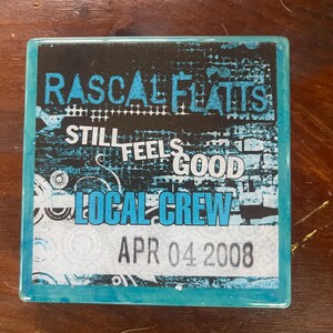 Può includere: Un biglietto commemorativo quadrato blu e nero con il testo "Rascal Flatts Still Feels Good Local Crew" e la data "APR 04 2008".