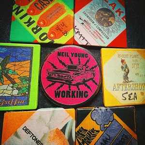 May include: A collection of nine colorful concert ticket stubs, featuring bands like Neil Young, Robert Plant, and Def Leppard. The tickets are rectangular and have a variety of designs, including a pink ticket with a black car and lightning bolts, a yellow ticket with a cartoon character, and a blue ticket with a band name.