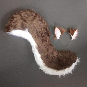 May include: A brown and white furry tail with a white tip and a headband with brown furry ears with pink insides.