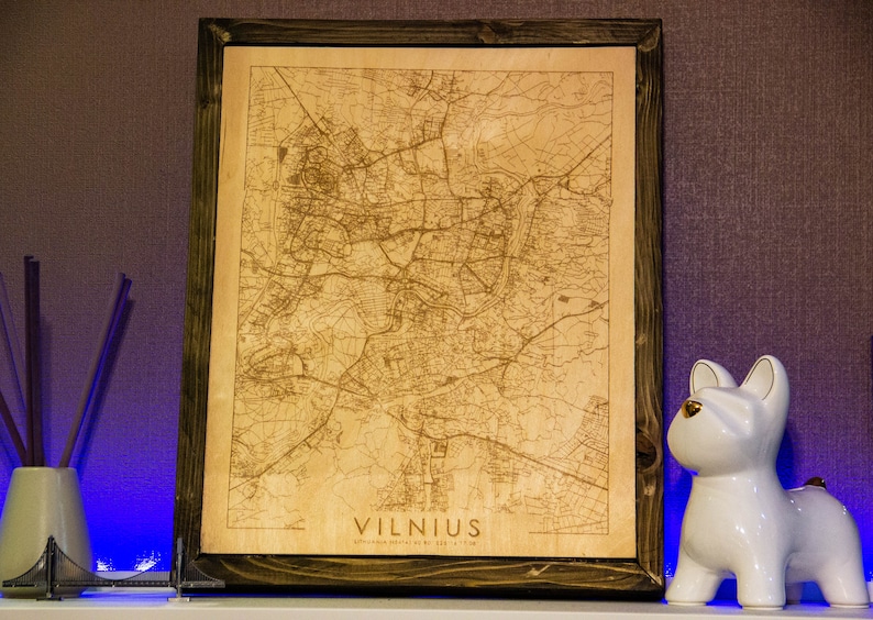May include: A wooden framed map of Vilnius, Lithuania, with a detailed street map engraved on the wood. The map is in a brown frame and has the word "VILNIUS" printed in the bottom right corner.