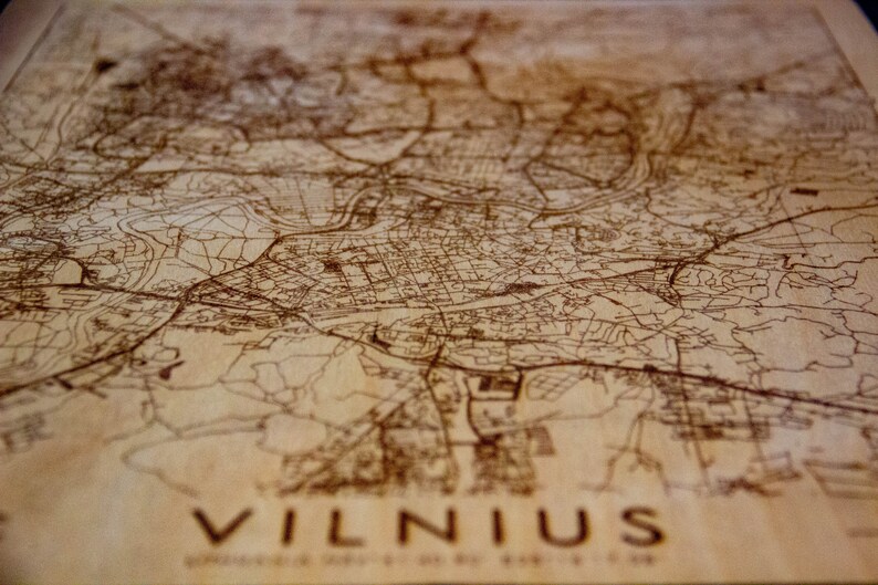 May include: A wooden map of Vilnius, Lithuania, with brown lines representing streets and waterways. The map is engraved with the word "VILNIUS" at the bottom.