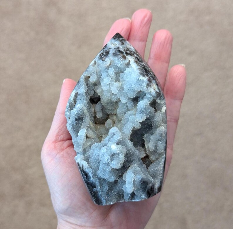May include: A gray and white crystal point with a unique, textured surface. The crystal has a pointed top and a flat base.
