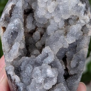 May include: A geode with a gray exterior and a white, crystal-lined interior. The crystals are clustered together in a variety of shapes and sizes.