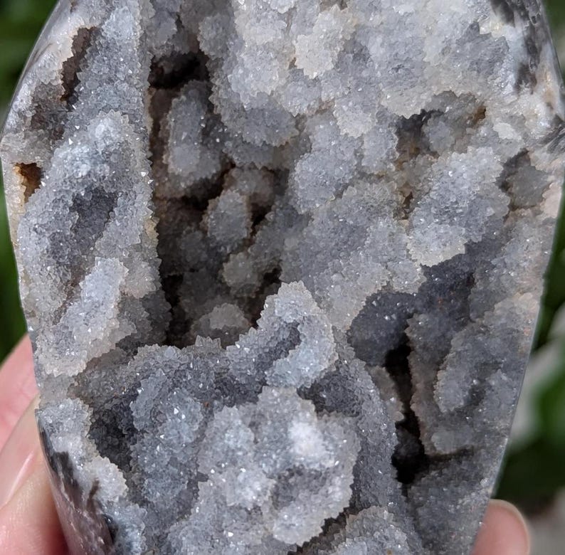 May include: A geode with a gray exterior and a white, crystal-lined interior. The crystals are clustered together in a variety of shapes and sizes.