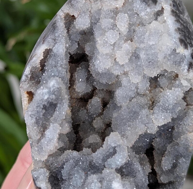 May include: A close-up of a gray and white agate geode with a crystal-lined interior. The geode has a rough, natural exterior and a smooth, polished interior.