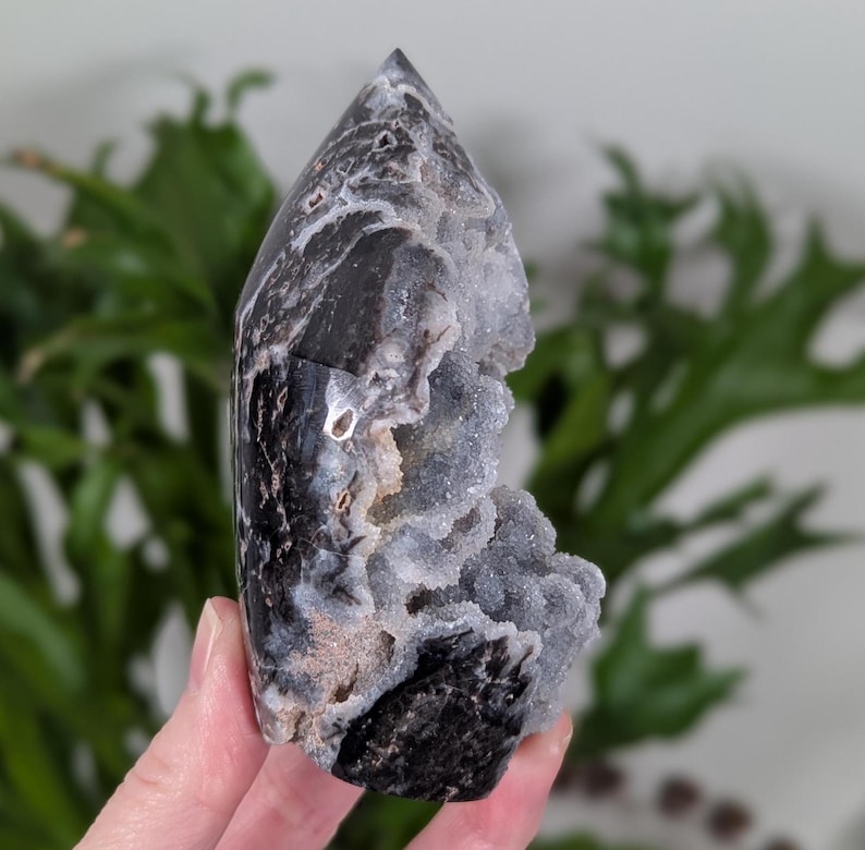 May include: Black and white agate crystal point with a natural druzy formation. The crystal has a pointed tip and a rough, textured surface.