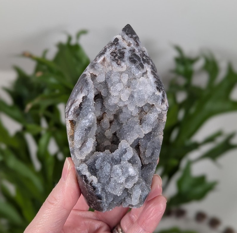 May include: A gray and white crystal with a druzy surface. The crystal is shaped like a point and has a natural, rough texture.