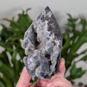 May include: A black and white agate geode with a cluster of white crystals inside. The geode is shaped like a point and has a rough, natural texture.