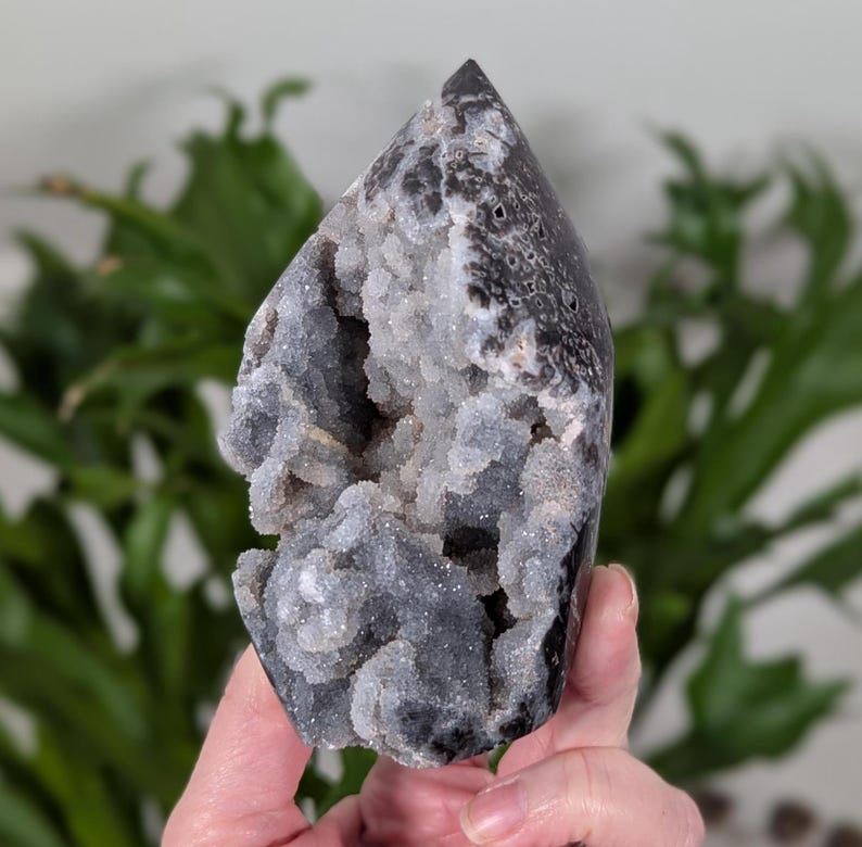 May include: A black and white agate geode with a cluster of white crystals inside. The geode is shaped like a point and has a rough, natural texture.