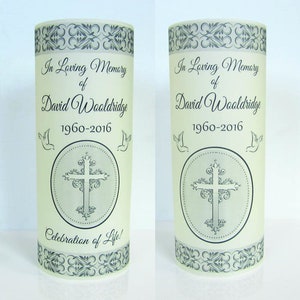 May include: Two white frosted glass candle holders with black decorative borders and a cross design. The text "In Loving Memory of David Wooldridge 1960-2016" and "Celebration of Life!" is printed on the candle holders.