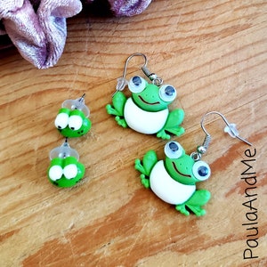 May include: A pair of green frog earrings. One pair is a stud earring with a small green frog charm. The other pair is a dangle earring with a larger green frog charm.