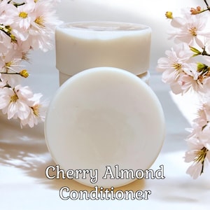 May include: Three white solid bars of Cherry Almond Conditioner. The bars are stacked on top of each other. The background is white with pink cherry blossoms.