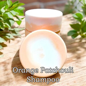 May include: Three round bars of orange and white shampoo soap stacked on top of each other. The soap is labeled "Orange Patchouli Shampoo".