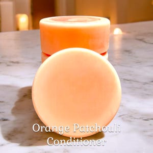 May include: Three round bars of orange-colored solid conditioner stacked on top of each other. The label reads "Orange Patchouli Conditioner".