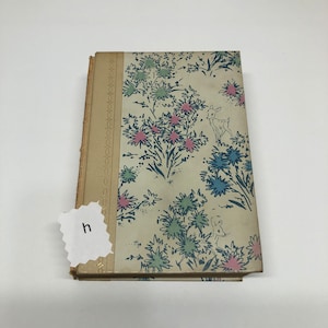 May include: A vintage book with a cream-colored cover featuring a floral pattern in shades of blue, pink, and green. The book has a decorative border on the spine.