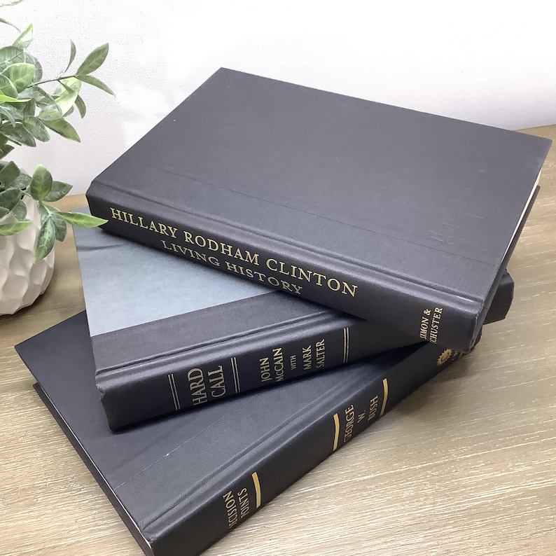 K&ouml;nnte beinhalten: Drei gebundene B&uuml;cher, die &uuml;bereinander gestapelt sind. Das oberste Buch ist schwarz mit goldenen Lettern, auf denen "Hillary Rodham Clinton Living History" steht. Das mittlere Buch ist schwarz mit goldenen Lettern, auf denen "Hard Call John McCain with Mark Salter" steht. Das unterste Buch ist schwarz mit goldenen Lettern, auf denen "Decision Points George W. Bush" steht.