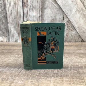May include: A vintage green hardcover book titled "Second Year Latin" by Scudder. The cover features an illustration of a group of people in medieval garb.