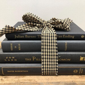 Pu&ograve; includere: Una pila di quattro libri grigio scuro legati con un nastro a scacchi bianco e nero. I libri hanno lettere dorate e includono titoli come "Julian Barnes The of an Ending" e "Terror in Berlin."