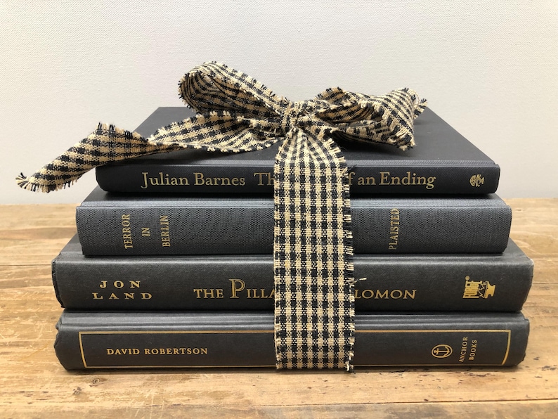 Pu&ograve; includere: Una pila di quattro libri grigio scuro legati con un nastro a scacchi bianco e nero. I libri hanno lettere dorate e includono titoli come "Julian Barnes The of an Ending" e "Terror in Berlin."