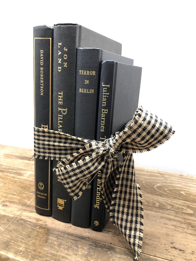 Pu&ograve; includere: Un gruppo di quattro libri neri legati con un nastro a quadretti neri e beige. I titoli dei libri includono "David Robertson", "Jon Land The Pillar", "Terror in Berlin" e "Julian Barnes T". I libri sono su una superficie di legno.