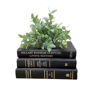 K&ouml;nnte beinhalten: Ein Stapel von drei schwarzen Hardcover-B&uuml;chern mit goldenen Lettern. Das oberste Buch ist "Living History" von Hillary Rodham Clinton. Das mittlere Buch ist "Hard Call" von John McCain. Das unterste Buch ist "Decision Points" von George W. Bush. Eine kleine gr&uuml;ne Pflanze sitzt auf den B&uuml;chern.