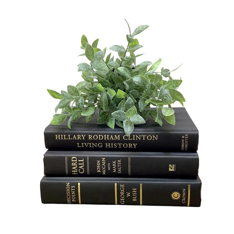 K&ouml;nnte beinhalten: Ein Stapel von drei schwarzen Hardcover-B&uuml;chern mit goldenen Lettern. Das oberste Buch ist "Living History" von Hillary Rodham Clinton. Das mittlere Buch ist "Hard Call" von John McCain. Das unterste Buch ist "Decision Points" von George W. Bush. Eine kleine gr&uuml;ne Pflanze sitzt auf den B&uuml;chern.