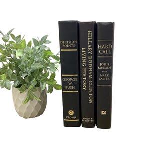 K&ouml;nnte beinhalten: Drei schwarze Hardcover-B&uuml;cher mit goldenen Schriftz&uuml;gen auf den Buchr&uuml;cken. Die Titel lauten "Decision Points" von George W. Bush, "Living History" von Hillary Rodham Clinton und "Hard Call" von John McCain mit Mark Salter.