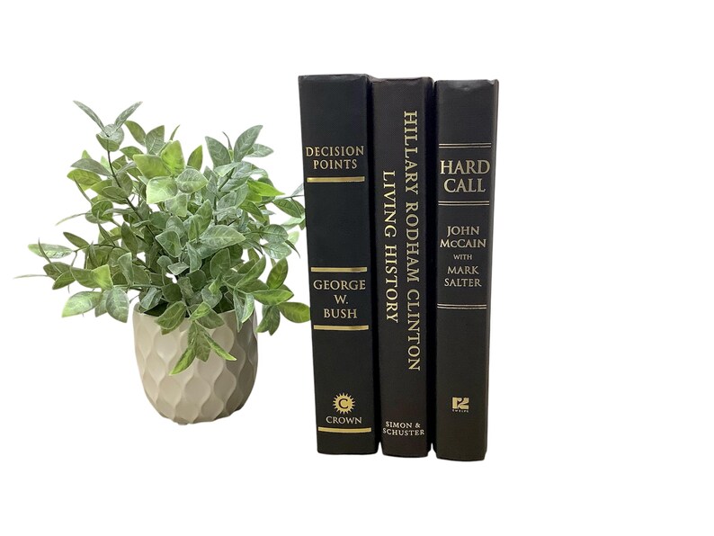 K&ouml;nnte beinhalten: Drei schwarze Hardcover-B&uuml;cher mit goldenen Schriftz&uuml;gen auf den Buchr&uuml;cken. Die Titel lauten "Decision Points" von George W. Bush, "Living History" von Hillary Rodham Clinton und "Hard Call" von John McCain mit Mark Salter.