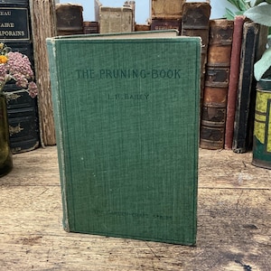 May include: A vintage green hardcover book titled The Pruning-Book by L.H. Bailey from The Garden-Craft Series. The front cover features dark green embossed text on a textured fabric material, standing upright with a worn, aged appearance.