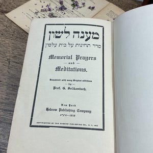 May include: An open book with off-white pages featuring a title page printed in black ink. The text includes Hebrew characters and English words: Memorial Prayers and Meditations, Translated with many Original additions by Prof. G. Selikovitsch.