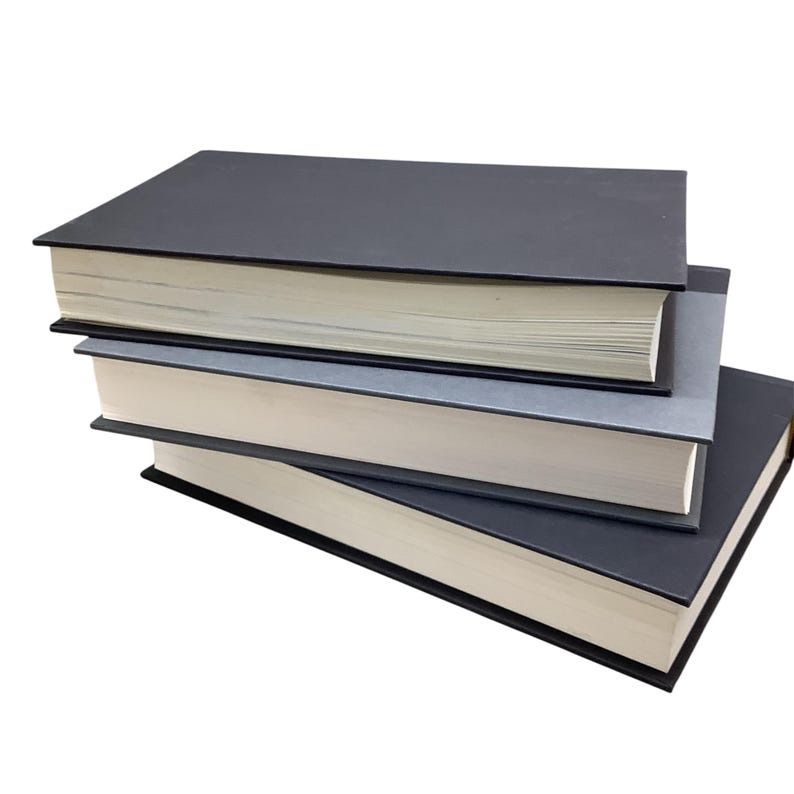 K&ouml;nnte beinhalten: Ein Stapel von drei gebundenen B&uuml;chern mit schwarzen und grauen Einb&auml;nden. Das oberste Buch ist schwarz, das mittlere Buch ist grau und das unterste Buch ist schwarz.