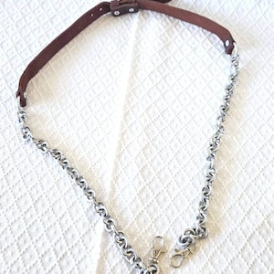 May include: A brown leather and silver chain purse strap. The strap has a brown leather section with a buckle and silver chain links. The chain ends with two silver clasps.