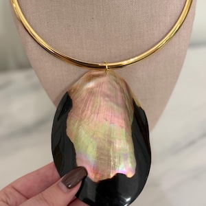 May include: A gold-tone choker necklace with a large, iridescent pendant. The pendant is a mix of black and pearlescent colors, with a shell-like appearance. The necklace is displayed on a neutral-colored mannequin.