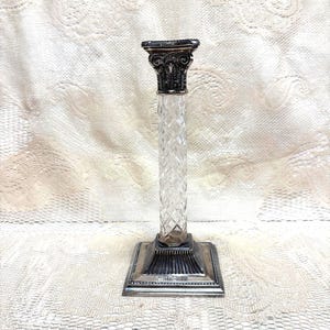 May include: A clear glass candlestick with a diamond pattern column and a silver-colored base and top. The top has an ornate design. The candlestick is a decorative item.