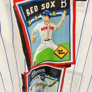 May include: A white fabric with blue stripes features a repeating pattern of baseball cards. The cards feature different baseball players in their uniforms. One card features a player in a red uniform with the text "RED SOX B" on the card. Another card features a player in a blue uniform with the text "Brewers" on the card.