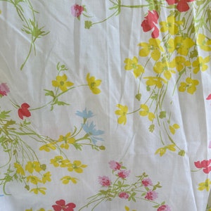 May include: White fabric with a floral pattern featuring yellow, pink, red, and blue flowers. The flowers are scattered across the fabric and have a delicate, vintage look.