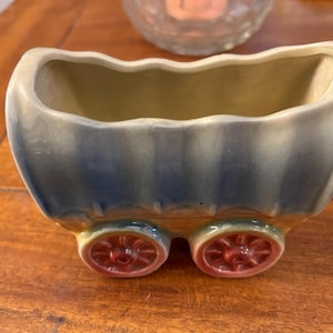 May include: A blue and green ceramic planter shaped like a covered wagon with red wheels.