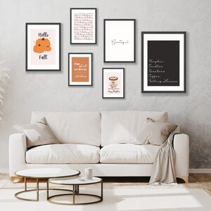 May include: A collection of framed art prints with fall-themed designs. The prints feature text like "Hello Fall" and "Grateful", along with images of pumpkins and fall-related items. The frames are black, and the art is displayed above a white sofa.