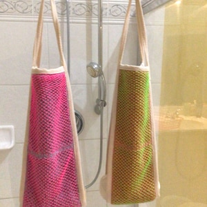 May include: Two mesh laundry bags hanging from a shower rod. The bag on the left is pink and the bag on the right is green.