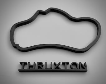 以下が含まれることがあります： Thruxton モータースポーツトラックの黒色の3Dプリントモデル。トラックは単一レーンで閉じたループです。トラックの下に「Thruxton」という名前が印刷されています。