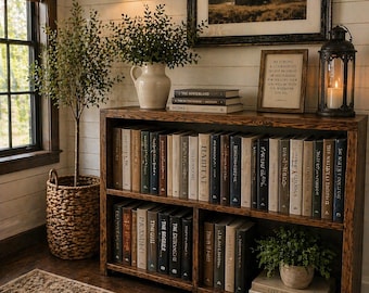 May include: A rustic wooden bookshelf filled with books, a framed landscape print, and decorative items. The shelves are stained a warm brown, and the books have various colored spines. A small potted plant and a lantern with a lit candle add to the cozy atmosphere.