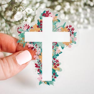 May include: A white cross with floral details in shades of red, green and yellow. The cross is surrounded by a border of flowers.