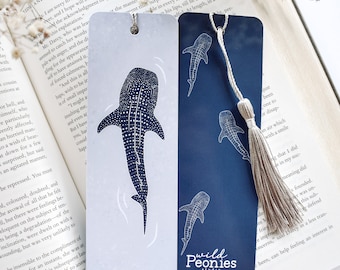 May include: Two bookmark designs featuring a whale shark illustration. The first bookmark has a white background with a blue whale shark. The second bookmark has a dark blue background with three blue whale sharks. Both bookmarks have a white tassel.