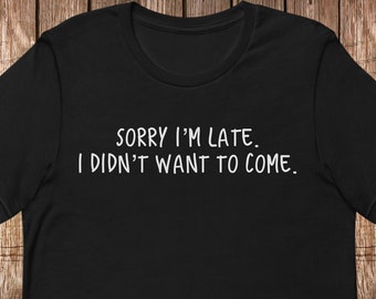 May include: A black short-sleeved t-shirt featuring the white printed text "SORRY I'M LATE. I DIDN'T WANT TO COME." centered on the chest. The garment has a crew neckline and a standard fit, showcasing a simple design with bold, legible lettering.