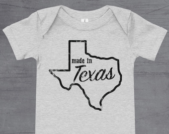 May include: A grey short-sleeved baby onesie with a black outline of the state of Texas and the text "made in Texas" inside the outline.